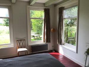 una camera da letto con tre finestre, una sedia e un tavolo di Farmhouse Okkingastate a Wijnaldum