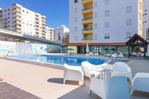 a swimming pool with white chairs and tables and buildings at Rocha Retreat - Praia Da Rocha in Portimão