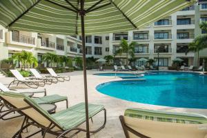 a swimming pool with chairs and an umbrella next to a hotel at PC209 - Pool View - Perfect for families or group - Close to Palm Beach - 2BR in Palm-Eagle Beach