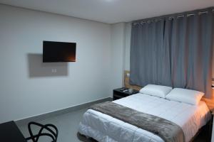 a hotel room with a bed and a flat screen tv at Dicopi Hotel in Maringá