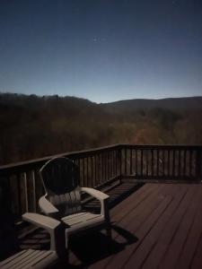 a chair sitting on a deck with a view at Log Cabin w Fireplace, EV Station & River Access in Great Cacapon