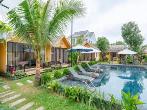 a pool with a palm tree and chairs and umbrellas at Winhouse Villa in Hoi An
