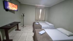 a room with two beds and a desk and a television at Hotel do Vale in Juscimeira
