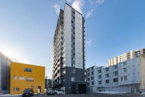 a tall building in a parking lot next to buildings at Cozy Stay Sapporo Hongodori 405 in Sapporo