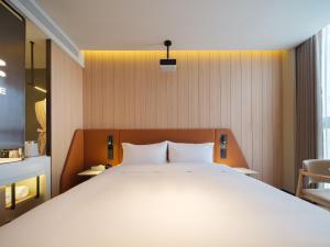a bedroom with a large white bed and a chair at 桔作酒店 新乡东站市政府店 in Xinxiang