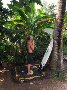 a man standing next to a surfboard next to a tree at Suna's Place in Ahangama