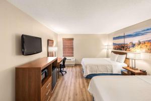 a hotel room with two beds and a desk with a television at Days Inn by Wyndham Raleigh-Airport-Research Triangle Park in Morrisville