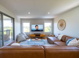 a living room with a brown couch and a flat screen tv at Chic Coastal Home on Orealla in Sunrise Beach