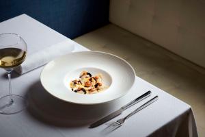 a white bowl of food on a table with a glass of wine at Tivoli Portopiccolo Sistiana Wellness Resort & Spa in Sistiana