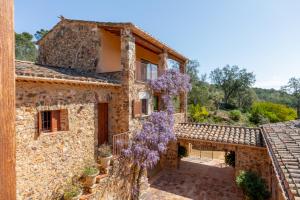 an exterior view of a stone house with a tree with purple flowers at Exquisite farmhouse in the Empordà Costa Brava in Vall-Llobrega