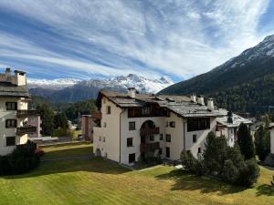 a building on a field with mountains in the background at Appartamento nuovo Sankt Moritz Chesa arlas 3B in St. Moritz