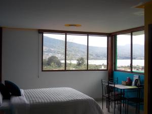 a bedroom with a bed and a table and windows at Green House Araque Inn in Otavalo