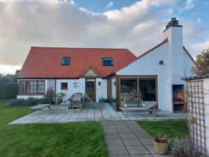 a white house with a red roof and a patio at Nivekerke 8 Nieuwmunster De Haan, 3-bedroom holiday house for 4 to 6 people, between Wenduine, 1 km, and De Haan, 2 km, 500 meters from the beach,15 min from Bruges, Ostend and Knokke, nice big fenced garden in Zuienkerke