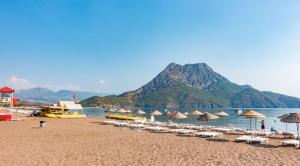 einen Strand mit Stühlen und Sonnenschirmen und einem Berg in der Unterkunft Cozy Mountain View House Near Olympos & Adrasan in Kumluca
