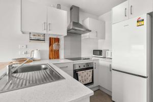 a white kitchen with a sink and a refrigerator at Coastal Bliss in Mount Maunganui