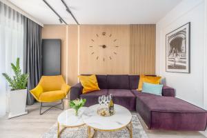 salon z fioletową kanapą i zegarem w obiekcie Apartamenty Fenomen - Premium Porto Nadmorskie Tarasy w Kołobrzegu w Kołobrzegu