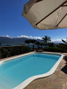 a large blue swimming pool with an umbrella at Chalés Mariolinha in Ilhabela