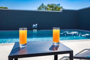 two glasses of orange juice sitting on a table next to a pool at Villa Marsel in Mednjan