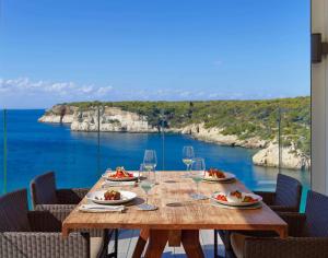 a wooden table with plates of food and wine glasses at Meliá Cala Galdana in Cala Galdana