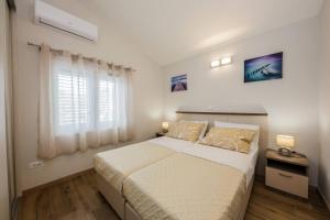 a white bedroom with a bed and a window at Apartmani Savin in Brodarica
