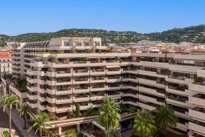 an apartment building with palm trees in front of a city at Hôtel Barrière Le Gray d'Albion in Cannes