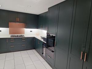 a kitchen with dark green cabinets and white tile floors at Forest Guest House in South Shields