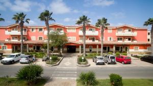 a large pink building with cars parked in a parking lot at Paraiso Tropical wifi and pool Djadsal moradias in Santa Maria