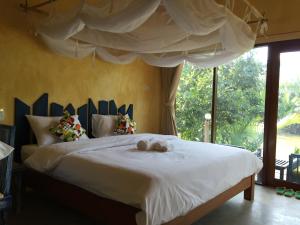 a bedroom with a large white bed with a window at Bangsrai Cottage in Surat Thani