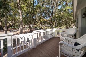 a porch with white railings and chairs and trees at 546 Tarpon Pond Cottage in Seabrook Island