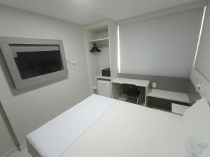 a white room with a bed and a desk and a tv at Trip Hotel Ubá - perto da Faculdade OZANAM COELHO e Eventos HORTO FLORESTAL in Ubá