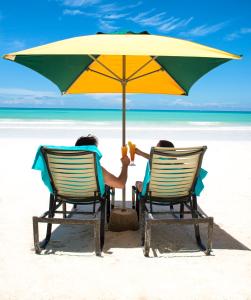 two people sitting in chairs under an umbrella on the beach at Acajou Beach Resort in Baie Sainte Anne