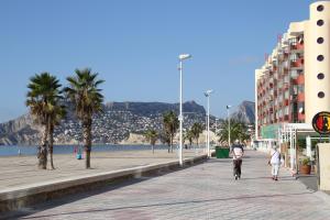 a beach with palm trees and people walking down a sidewalk at Amatista 12 D - Private in Calpe