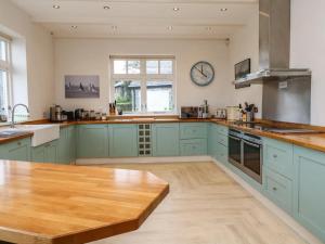 une cuisine avec des placards bleus et une table en bois dans l'établissement Penarvon House - Stunning Waterfront Escape with Games Room, à Manaccan