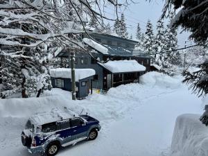 a blue car parked in the snow in front of a house at Bears Den Mountain Lodge in Hakuba
