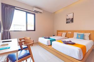 a bedroom with two beds and a desk and a table at Sans Hotel Bobosini Malang by RedDoorz in Malang