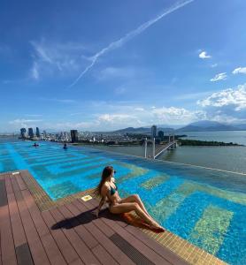 una donna seduta sul bordo di una piscina di Golden Bay Apartment Ocean View a Da Nang