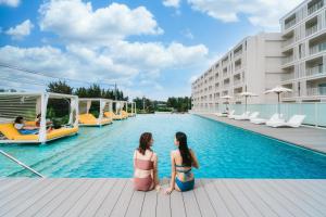 two women sitting on the edge of a pool at a hotel at BEB5 Okinawa Seragaki by Hoshino Resorts in Onna