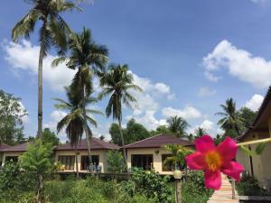 a house with palm trees and a pink flower at Bangsrai Cottage in Surat Thani