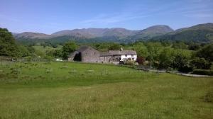 an old barn in a field with mountains in the background at High Wray Farm in Ambleside