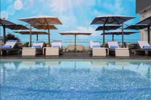 um grupo de cadeiras e guarda-sóis ao lado de uma piscina em Wink Icon Hotel Danang Riverside - Luxury Suites - 24hrs Stay & Rooftop Pool Bar em Da Nang