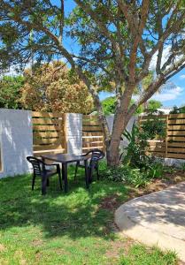 a picnic table and two chairs under a tree at Beach Walk Cottage in Plettenberg Bay