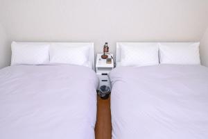 two beds with white sheets and a night stand between them at Bhome Hikone Jizo in Hikone