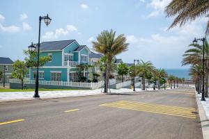 a blue house on a street with palm trees and the ocean at Nhà A Trí in Bình Tú