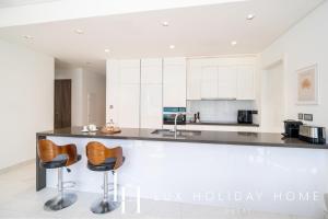 a kitchen with white cabinets and a counter with stools at LUX The District One Lagoon View Suite in Dubai