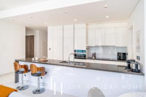 a kitchen with white cabinets and bar stools at LUX The District One Lagoon View Suite in Dubai