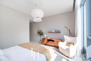a white bedroom with a bed and a chair at LUX The District One Lagoon View Suite in Dubai