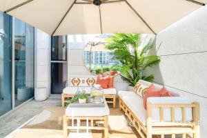 a patio with a couch and tables and an umbrella at LUX The District One Lagoon View Suite in Dubai