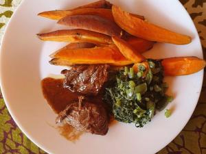 a plate of food with meat and vegetables on a table at Nxabii Cottages in Kasane