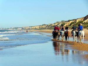 een groep mensen die op paarden op het strand rijden bij Tu casa en Doñana in Matalascañas