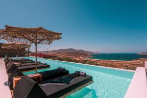 a pool with chairs and umbrellas and the ocean at Aora Villa Ftelia Beach Mykonos in Panormos Mykonos